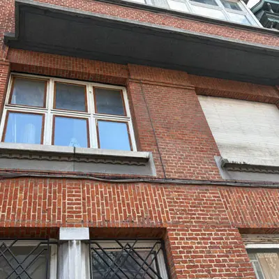 Volets en bois manuel avant remplacement, cadre bois apparent et lames fatiguées, premier étage à Schaerbeek